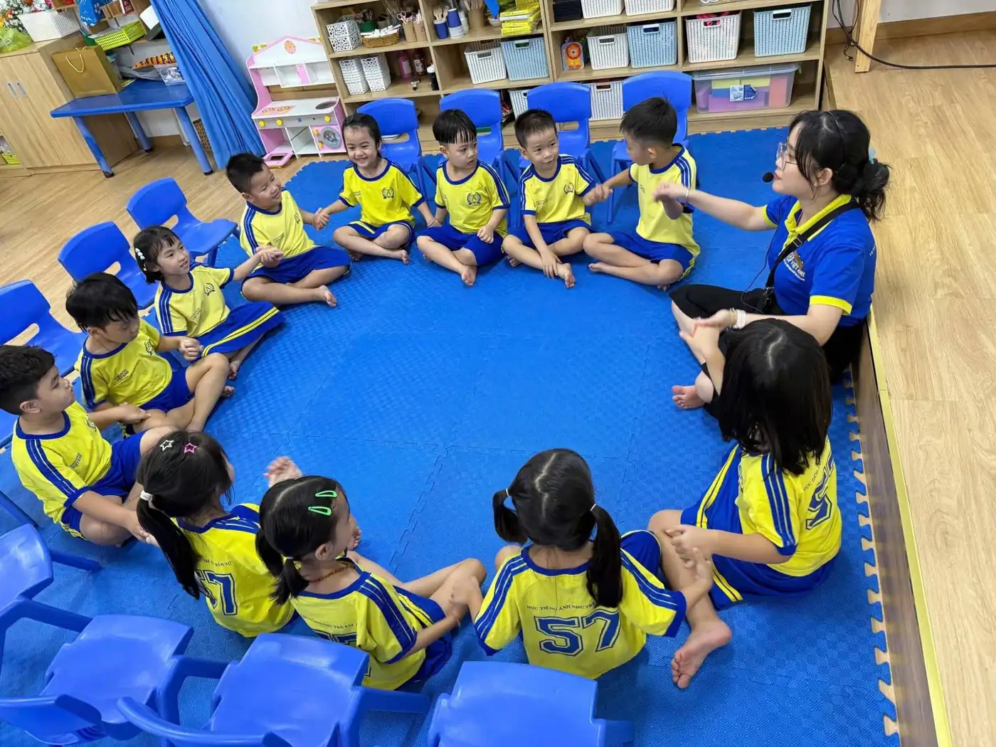 Cô giáo hướng dẫn trẻ lớp Lá ngồi thành vòng tròn, các bạn nhìn nhau và mỉm cười
