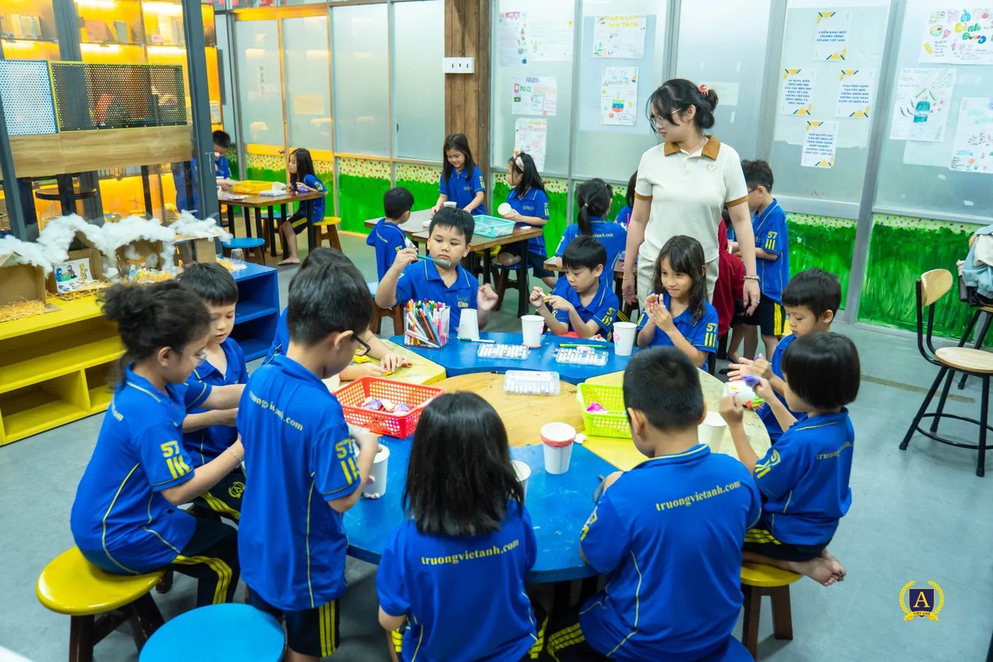 Phòng học STEAM-E với các bàn tròn, học sinh làm việc theo nhóm, giáo viên đi giữa các bàn quan sát