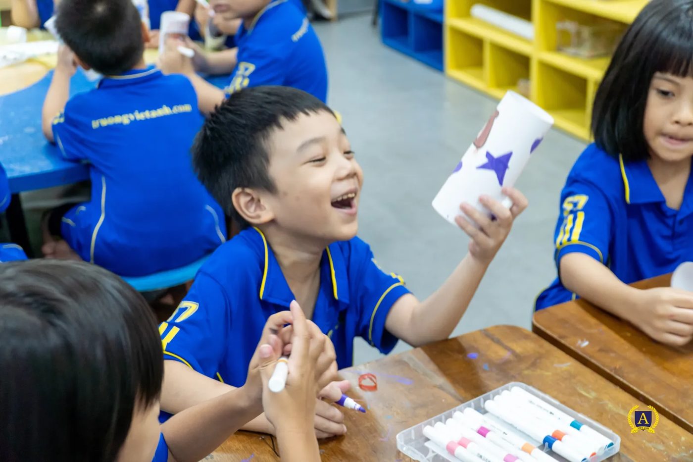 Một học sinh cười lớn khi cầm ống giấy tự cuộn vừa phóng lên, bạn ngồi cạnh nhìn theo